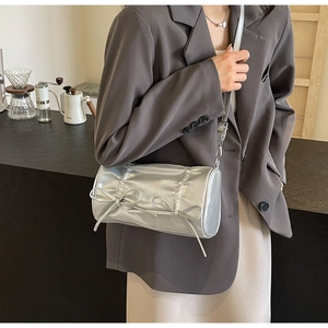 Detail of silver cylindrical crossbody bag with metallic sheen and bow accents on a model