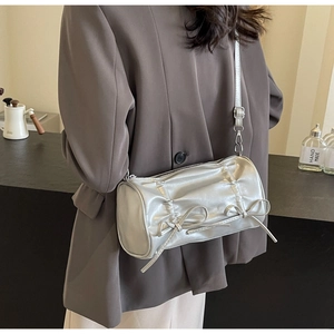 Silver pleated cylindrical crossbody bag with bow accents worn by model in gray blazer