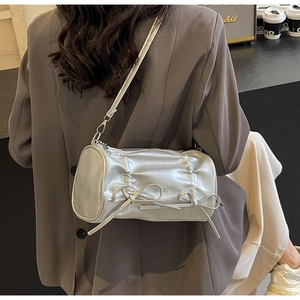 Silver pleated cylindrical crossbody bag featuring decorative bows on a model