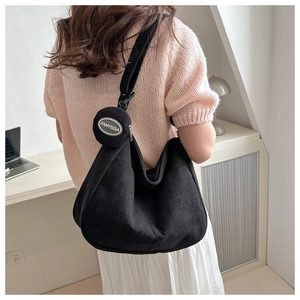 Detailed texture of black corduroy tote with a detachable mini logo pouch on a shoulder strap