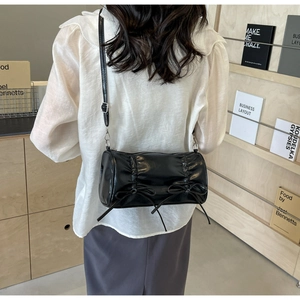 Detailed view of black pleated cylinder bag with bow accents and silver hardware
