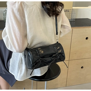 Detail of black barrel bag featuring decorative bows and pleated faux leather texture