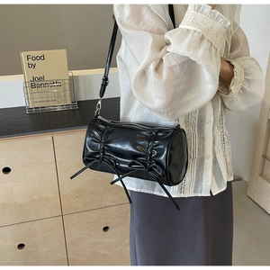 Detail of black pleated cylinder bag featuring bow accents and silver zipper hardware