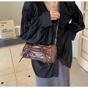 Detail of a dark brown pleated cylinder bag with bows and sleek faux leather finish