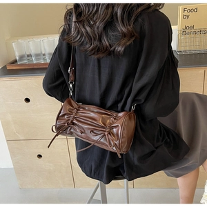 Detail of dark brown cylinder pillow bag with pleated leather and bow accents