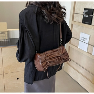 Detail view of a dark brown pleated cylinder bag with side bow detail and thin strap
