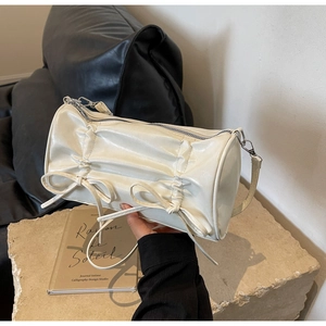 Detail view of the elegant pleated cream cylinder bag with delicate double bow accents