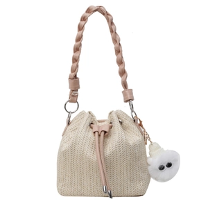 Large woven straw bucket bag with pink braided handle and plush charm for beach vacation