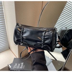Detail of black cylindrical pillow bag with vertical pleats and sweet bow accents