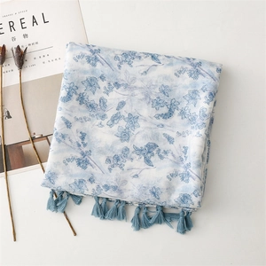 Close-up of light blue floral scarf with tassel fringe on a minimalist magazine background