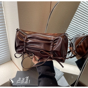Close-up of pleated dark brown cylinder bag with bow detail and glossy leather texture