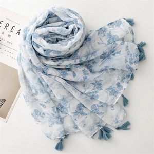 Detail of white cotton linen scarf with blue floral prints and tassel edges