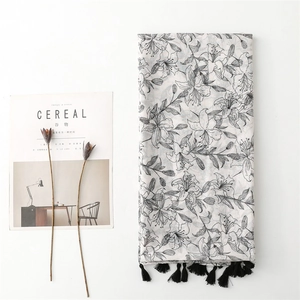 Détail d'une écharpe en lin avec motifs floraux noirs et finitions à pompons