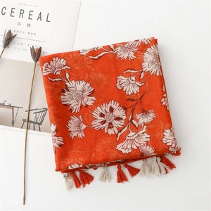 Flat lay of an orange cotton linen scarf with white floral patterns and fringe details