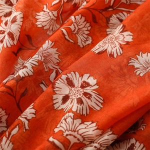 Close-up of bright orange linen-feel scarf fabric with detailed white floral patterns