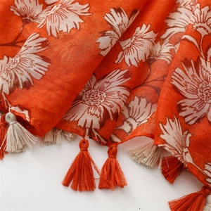 Detail of orange linen-feel scarf with white floral patterns and tassel edge decoration