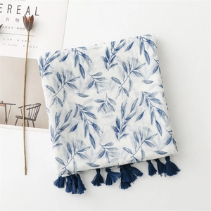 Close-up of blue leaf print scarf with tassels on white linen textured fabric