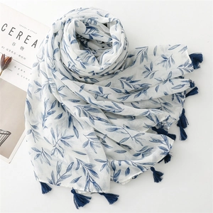 Detail of white cotton scarf with blue leaf patterns and fringed edges next to a magazine