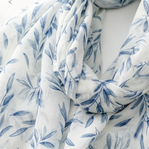 Close-up of white cotton scarf featuring blue leaf print and woven texture details