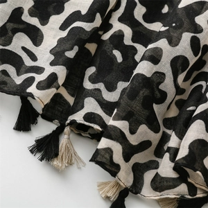 Detail of linen-feel scarf featuring black and white abstract patterns and fringe tassels
