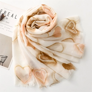 Detail of cream scarf with rose gold heart patterns and soft fringe edges on white table