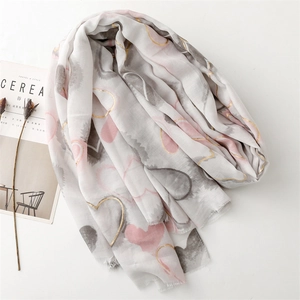 Detail of soft white scarf featuring pink and gold heart patterns and frayed edges