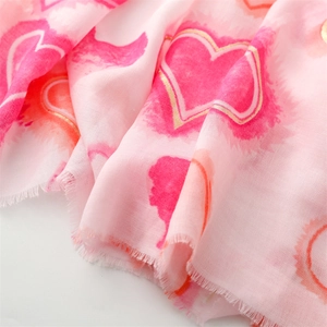 Detailed close-up of pink linen scarf with gold foil heart pattern and frayed edges