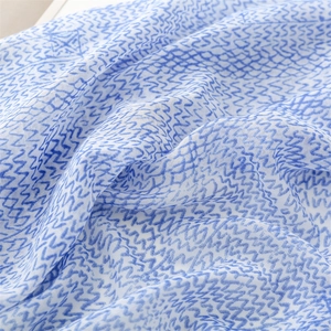 Detail of blue zigzag wave patterns on a lightweight white cotton linen scarf with tassels
