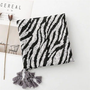 Detail of zebra and leopard print scarf with soft gray tassel fringe on a white surface