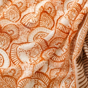 Close-up of linen-feel scarf featuring vintage orange floral patterns and soft tassel texture