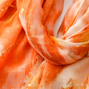 Close-up of orange gradient scarf featuring golden heart foil prints and pleated fabric