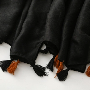 Close-up of black twill scarf fabric featuring vibrant black and orange fringe tassels
