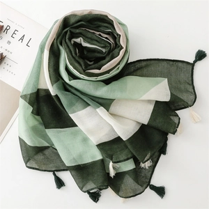 Detail of green and white striped lightweight scarf with decorative fringe on a white surface
