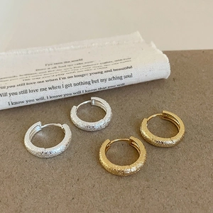 Close-up of geometric matte hoop earrings in gold and silver finish on vintage paper
