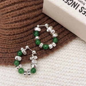 Detailed shot of handmade silver beads and green chalcedony hoop earrings on soft knit fabric