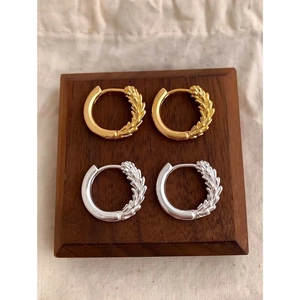 Golden and silver wheat ear hoop earrings displayed on wood with linen background