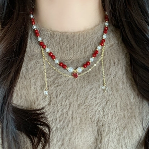 Elegant layered pearl necklace with red beads and three heart pendants on a brown sweater