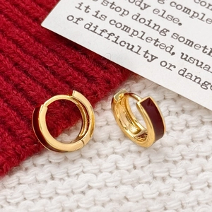 Créoles dorées minimalistes avec émail rouge foncé sur fond en tricot rouge vif