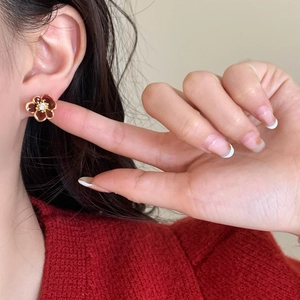 Red flower stud earrings with enamel petals and gold edging worn on an ear