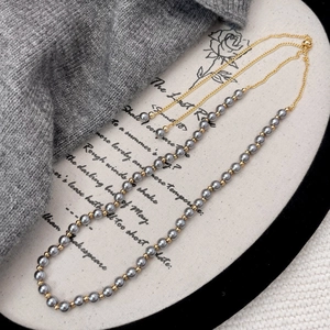 Detail of grey pearl necklace with golden spacer beads on a soft knit background