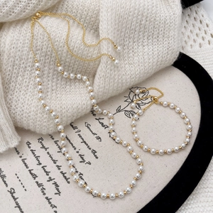 Elegant white pearl necklace and bracelet set with gold beads on a white knit sweater