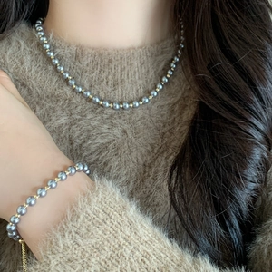 Elegant grey pearl necklace and bracelet set with gold beads on camel sweater background