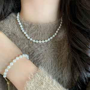 Elegant white pearl necklace and bracelet set with gold beads on a female model