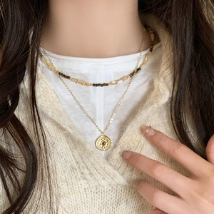 Close-up of layered tiger eye beaded necklace with sun totem coin pendant and gold chain