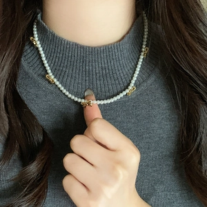 Elegante collana di perle bianche con fiocchi dorati su maglione antracite