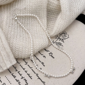 Dettaglio della collana di perle con fiocchi argentati su maglione lavorato a maglia