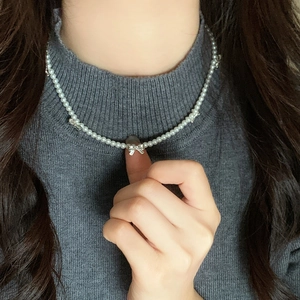 Elegante collana di perle bianche con ciondoli a fiocco argento su maglia grigia