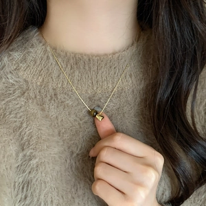 Detail of tiger eye bead and gold heart pendant on necklace worn with brown sweater
