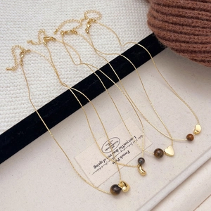 Four gold heart and tiger eye stone necklaces displayed on white and knit fabrics