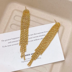 Eleganti orecchini a frangia dorati con lunghe nappe metalliche su una carta decorativa